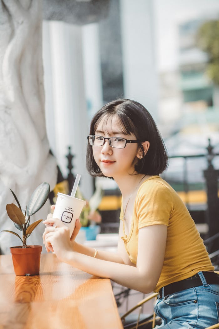 Beautiful woman in casual attire sipping a drink at a cozy cafe with natural light.