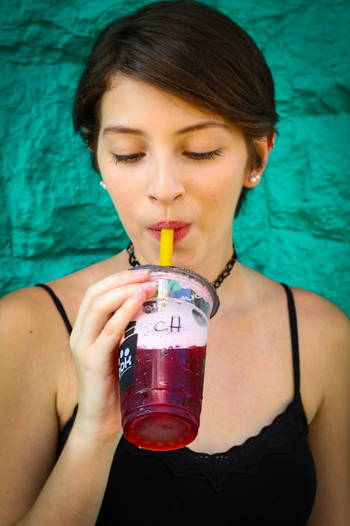 Young woman sipping a refreshing drink outdoors, showcasing vibrant colors against a textured backdrop.